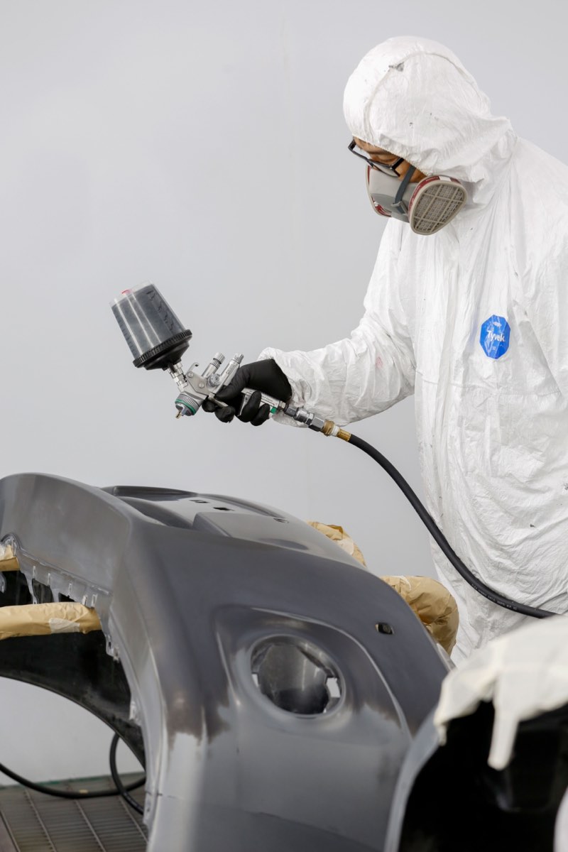 Técnico aplicando pintura a un parachoques en cabina de pintura